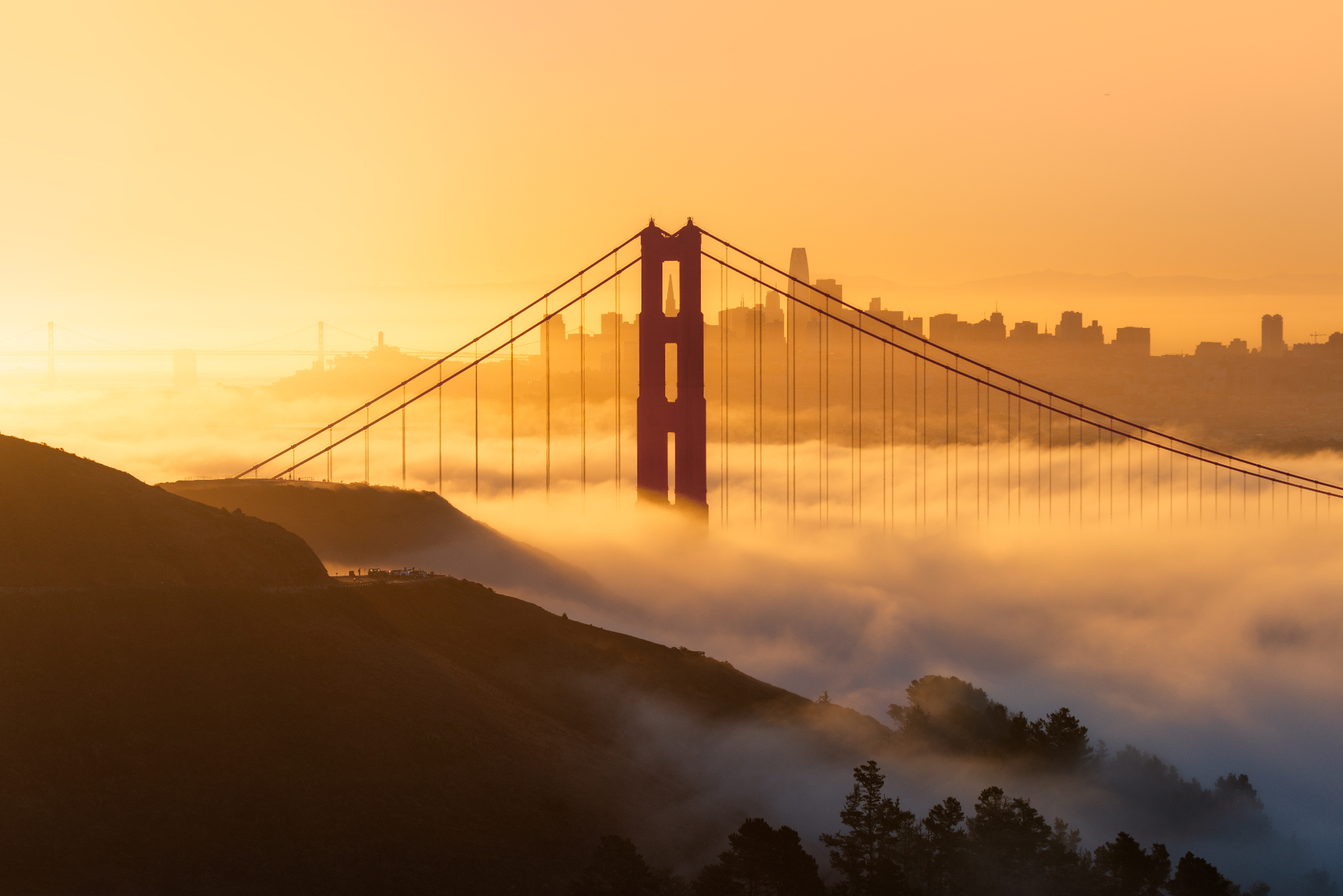 Golden Gate Bridge emerging through fog at sunrise with the San Francisco skyline