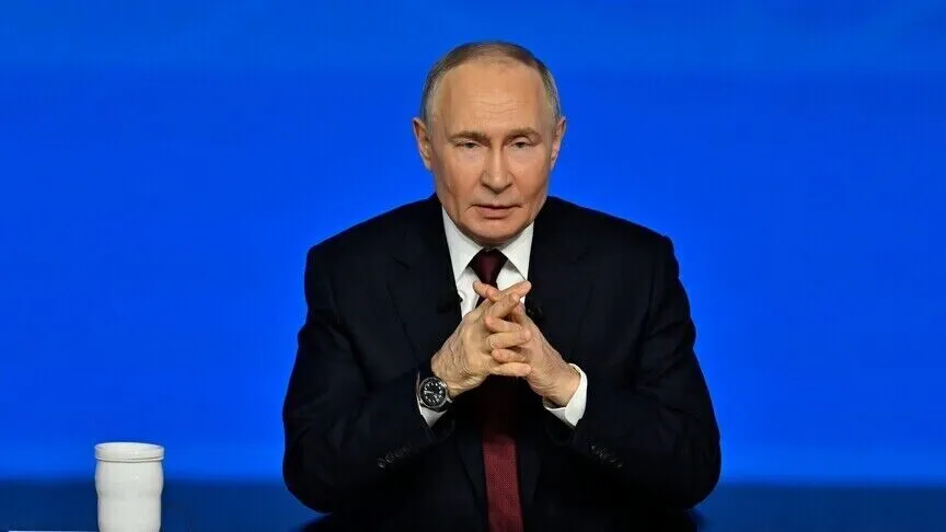 Vladimir Putin seated at a desk against a blue background