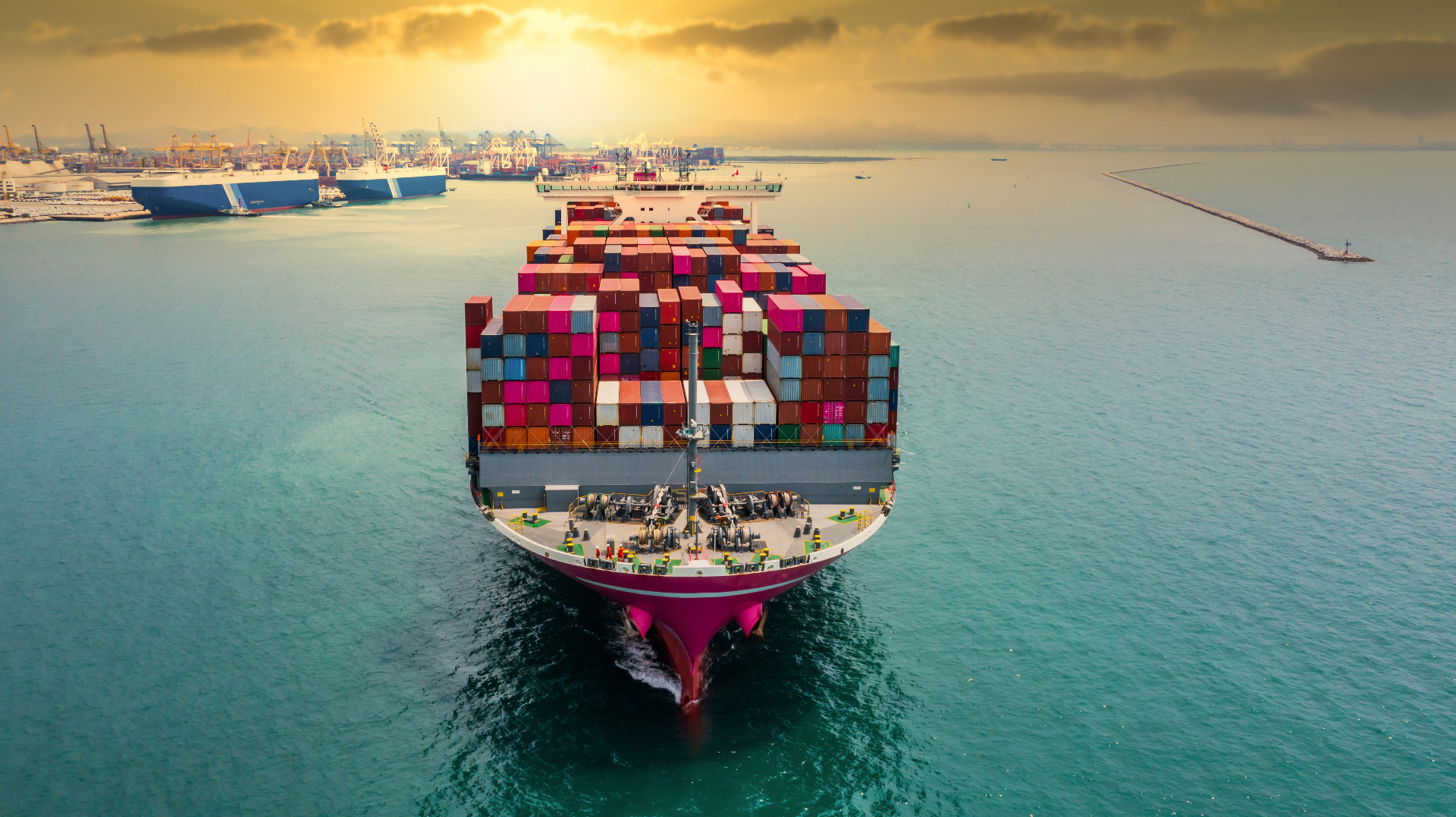 Container ship sailing toward port at sunset